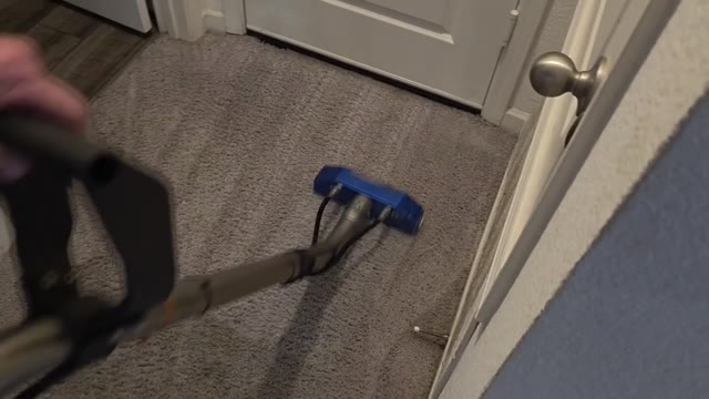 Steam-cleaning wand cleaning a residential hallway carpet up to a door